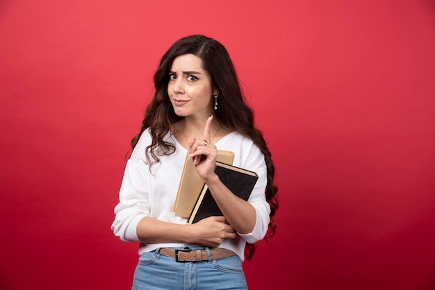 Donna castana che posa con il libro su fondo rosso. Foto di alta qualità