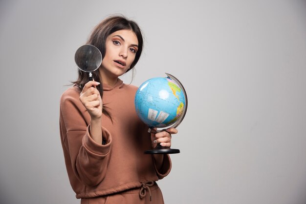 Donna castana che posa con la lente d'ingrandimento e il globo