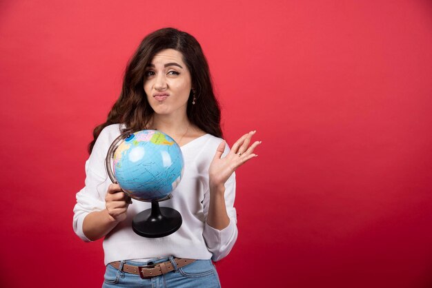 Donna castana che tiene il globo e fa la faccia. Foto di alta qualità