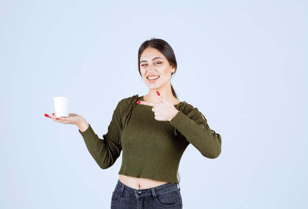 donna castana che tiene tazza di plastica e che indica.