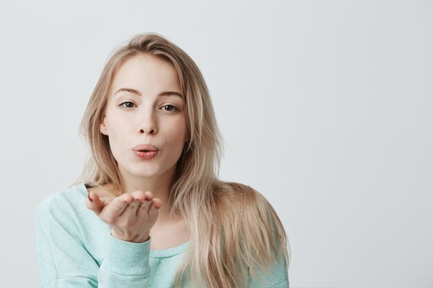 Donna caucasica attraente che posa con il bacio sulle sue labbra con capelli tinti biondi, avendo sguardo flirty sentirsi sicuri e belli.