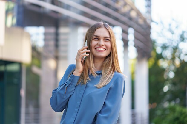 Donna caucasica di affari che parla dal caffè della tenuta del telefono per andare. Una donna europea di successo, parlando al telefono, in piedi su un moderno edificio per uffici