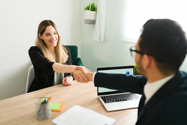 Donna caucasica felice che stringe la mano a un uomo latino durante un incontro di lavoro con un avvocato. Manager che assume una bella donna professionista per un nuovo lavoro