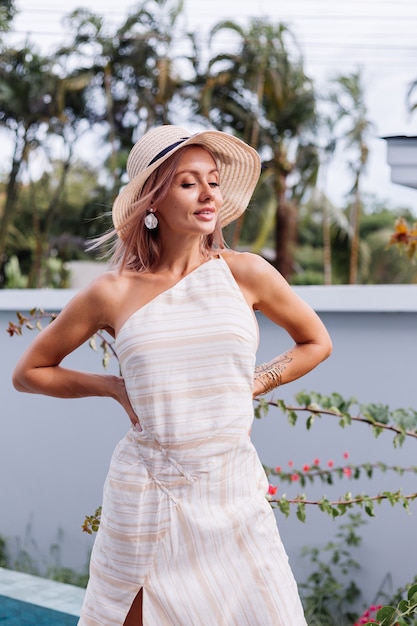 Donna caucasica romantica carina felice in abito bianco elegante con schiena scoperta e cappello di paglia