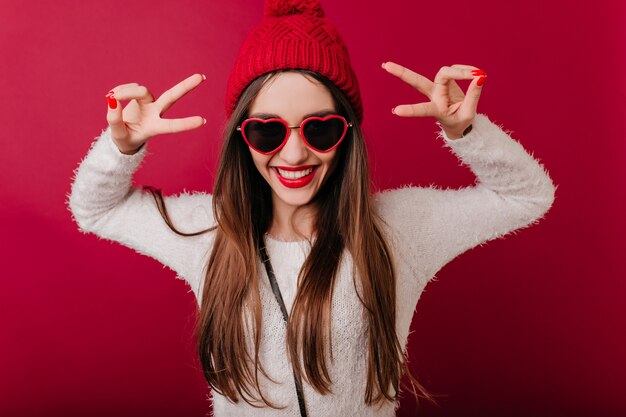 Donna caucasica spensierata in soffice maglione e cappello lavorato a maglia sorridente sullo spazio bordeaux