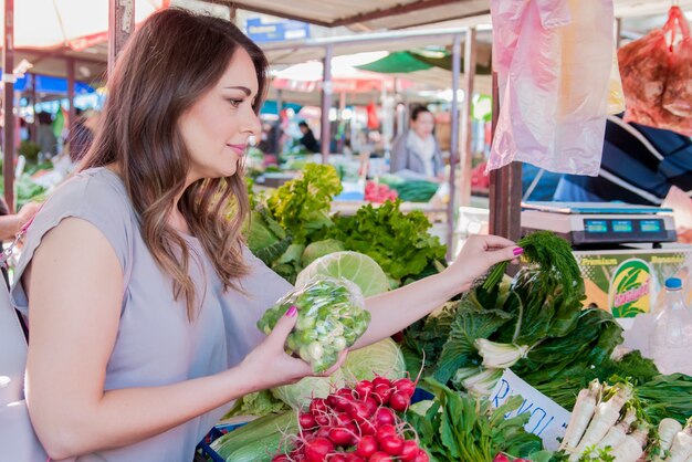 Donna che acquista verdure biologiche fresche al mercato di strada. Sorridente donna con verdure al negozio di mercato. Concetto di acquisto di alimenti sani