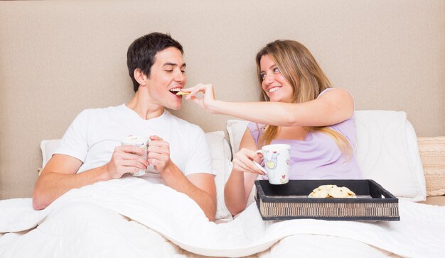 Donna che alimenta i biscotti al suo ragazzo seduto sul letto