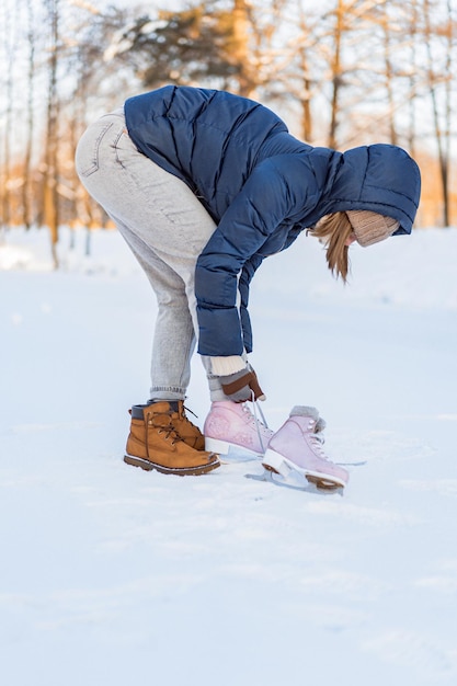 Donna che allaccia i pattini da ghiaccio sul bordo di un lago ghiacciato. Immagine ritagliata di una donna che indossa i pattini da ghiaccio. sport invernali, neve, divertimento invernale