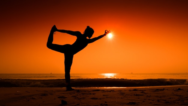 Donna che allunga il suo corpo in yoga pone al tramonto sulla spiaggia