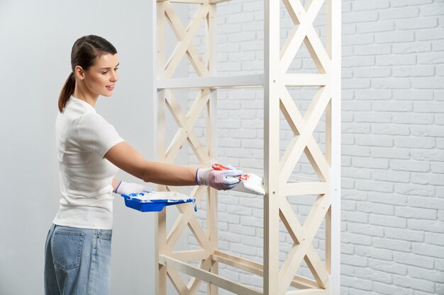 Donna che applica colore bianco con pennello su tavola di legno