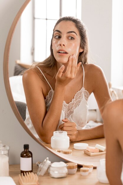 Donna che applica crema e che esamina lo specchio