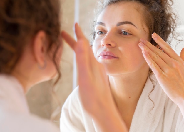 Donna che applica la crema sul viso mentre si guarda allo specchio