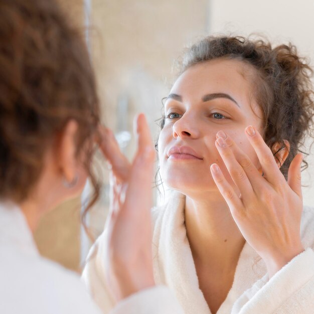 Donna che applica la crema sul viso mentre si guarda allo specchio