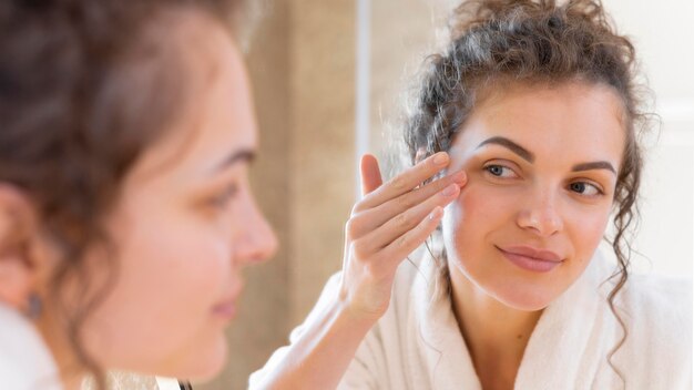 Donna che applica la crema sul viso mentre si guarda allo specchio