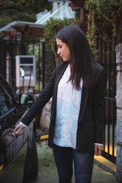 Donna che apre la portiera dell'auto elettrica alla stazione di ricarica del veicolo elettrico