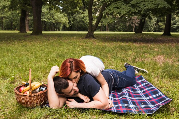 Donna che bacia il suo ragazzo che si trova sulla coperta sopra l&#39;erba verde nel parco