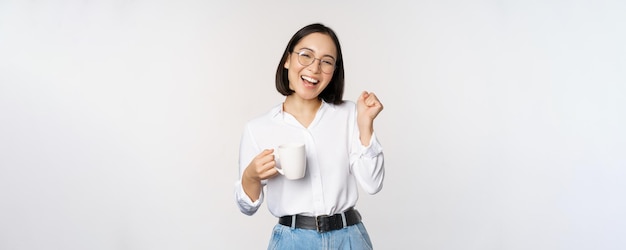 Donna che balla felice che beve caffè o tè dalla tazza Ragazza coreana con tazza in piedi su sfondo bianco