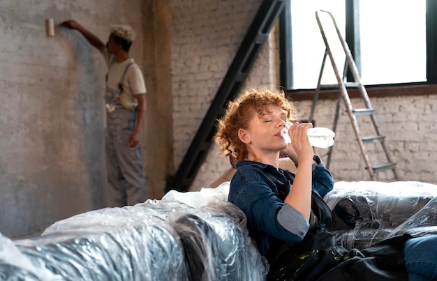 Donna che beve acqua mentre un uomo dipinge il muro della loro nuova casa