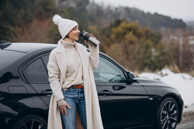 Donna che beve caffè con la sua macchina in piedi sulla strada nella foresta