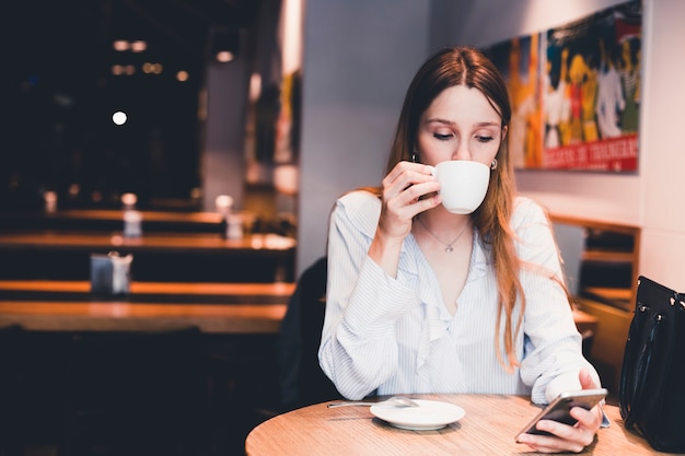 Donna che beve e usando smartphone