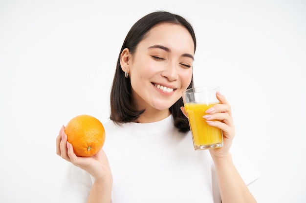 Donna che beve succo fresco con frutta arancione e sorride sentendosi sani e idratati studi bianchi