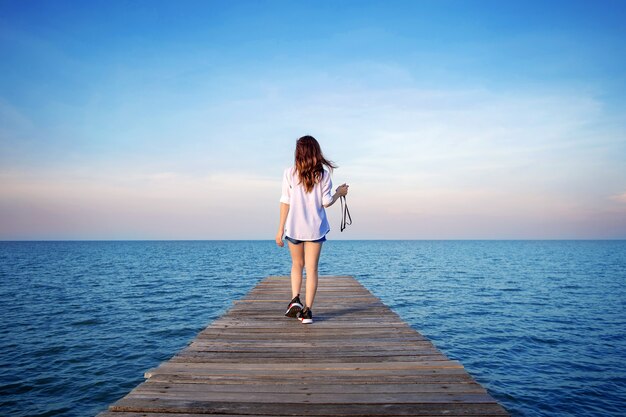 Donna che cammina sul ponte di legno esteso verso il mare.