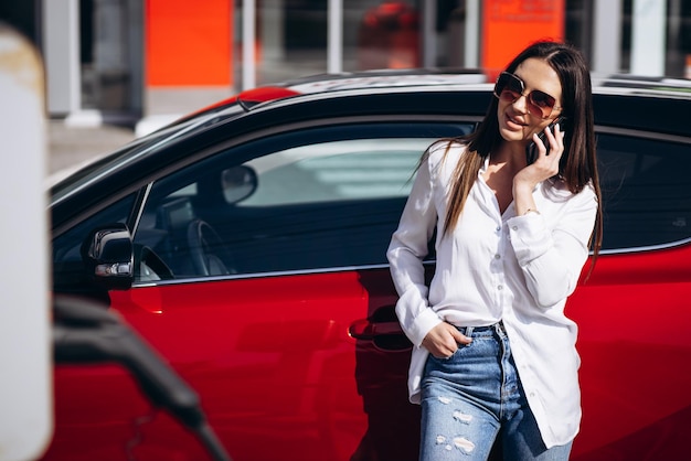 Donna che carica un'auto elettrica e parla al telefono