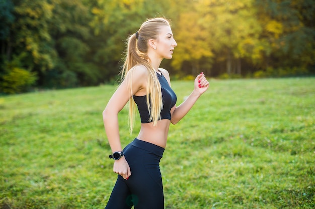 Donna che fa jogging in esecuzione nel parco sotto il sole in una bella giornata estiva. Modello di fitness sportivo allenamento di etnia caucasica all'aperto per la maratona.