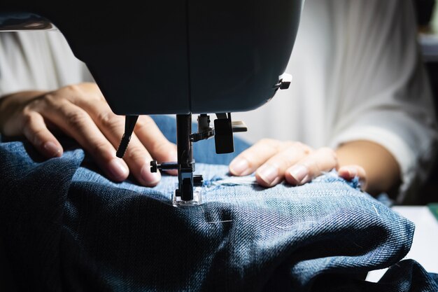 Donna che fa la rappezzatura dei jeans facendo uso della macchina per cucire - concetto di cucito domestico di DIY