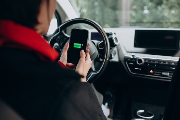 Donna che fa pagare la sua automobile e che esamina il cherger sul telefono del bher