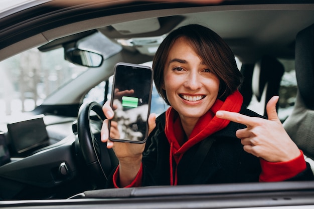 Donna che fa pagare la sua automobile e che esamina il cherger sul telefono del bher