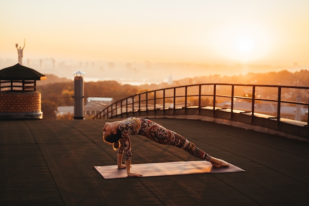 Donna che fa yoga sul tetto di un grattacielo in grande città.