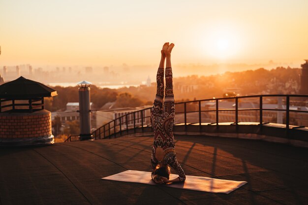 Donna che fa yoga sul tetto di un grattacielo in grande città.