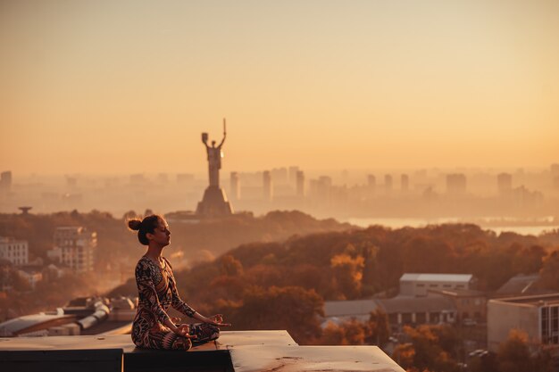 Donna che fa yoga sul tetto di un grattacielo in grande città.