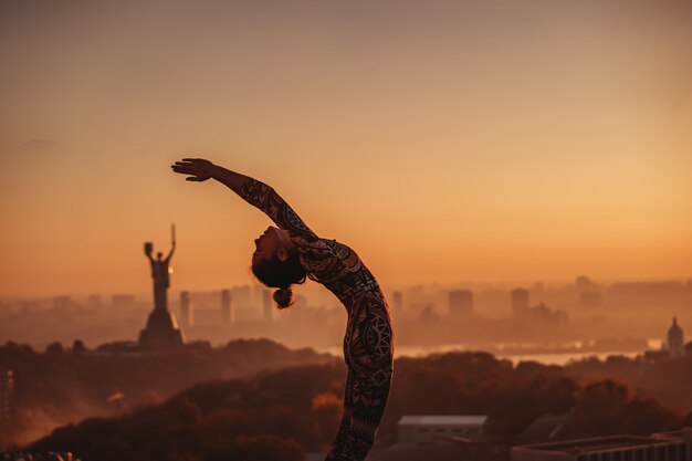 Donna che fa yoga sul tetto di un grattacielo in grande città.