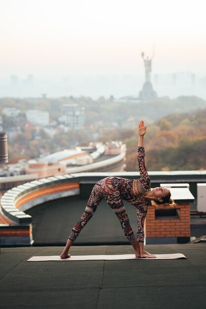 Donna che fa yoga sul tetto di un grattacielo in grande città.