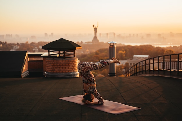 Donna che fa yoga sul tetto di un grattacielo in grande città.