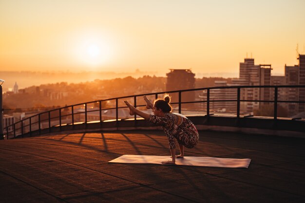 Donna che fa yoga sul tetto di un grattacielo in grande città.