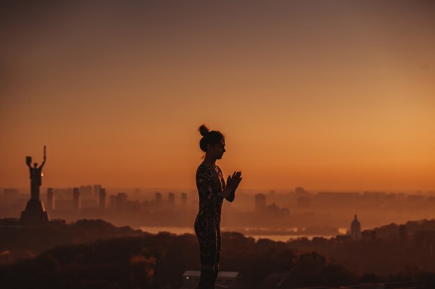 Donna che fa yoga sul tetto di un grattacielo in grande città.