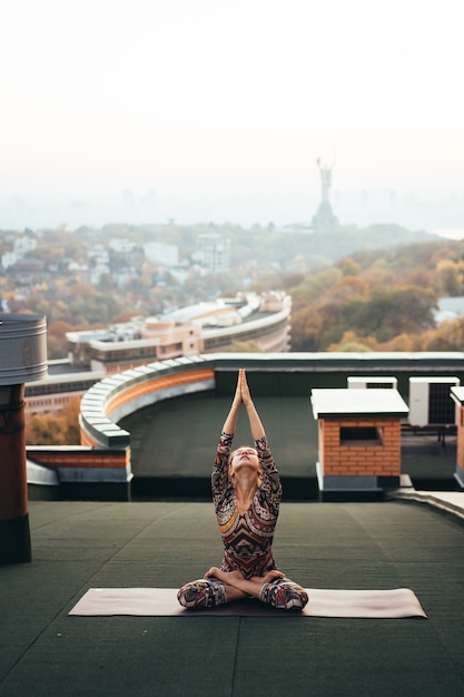 Donna che fa yoga sul tetto di un grattacielo in grande città.