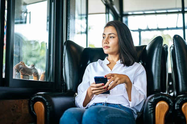 Donna che guarda fuori dalla finestra con lo smartphone in sua mano