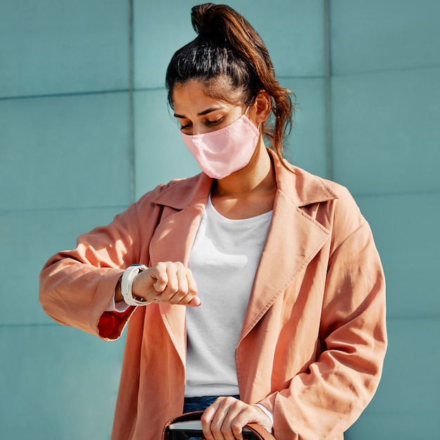 Donna che guarda il suo orologio mentre indossa una maschera medica durante una pandemia in aeroporto
