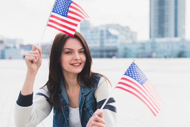 Donna che guarda l&#39;obbiettivo e sventolando bandiere americane nelle mani