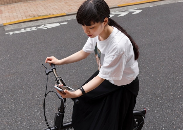 Donna che guida una bicicletta elettrica in città e tiene in mano uno smartphone