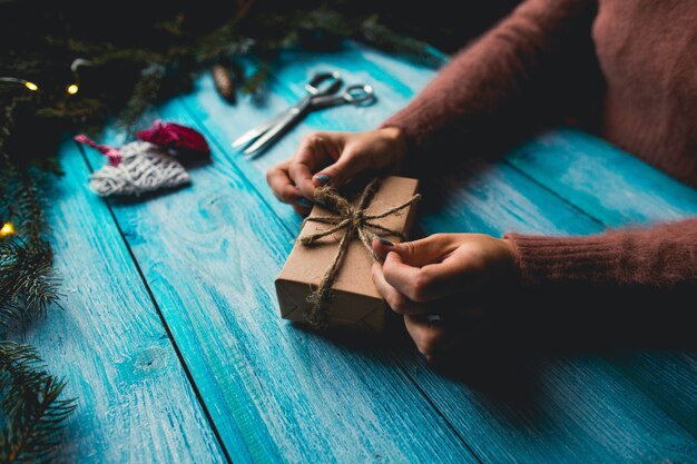 Donna che imballa un regalo di Natale su fondo di legno blu