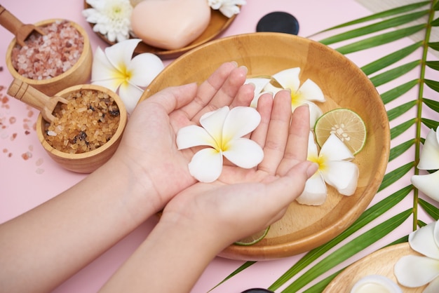 Donna che immerge le mani in una ciotola di acqua e fiori, trattamento Spa e prodotto per piedi femminili e spa per le mani, massaggio con ciottoli, acqua profumata di fiori e candele, relax. Lay piatto. vista dall'alto.