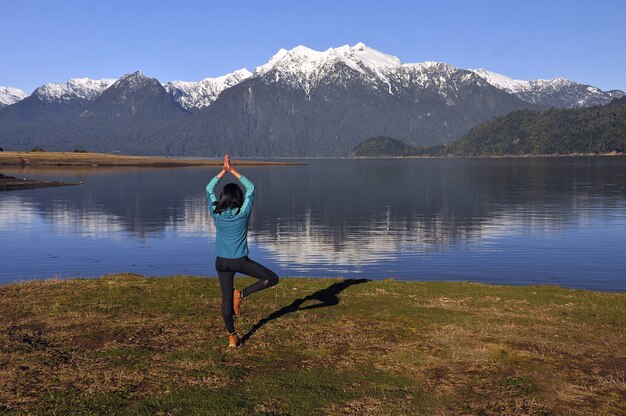 Donna che indossa abbigliamento sportivo, tenendo una posa yoga di fronte al lago calmo e alle montagne