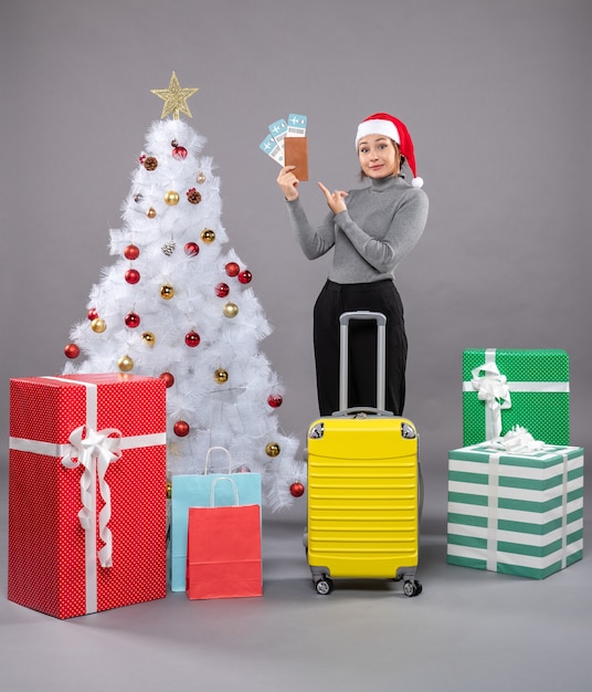 Donna che indossa il cappello di Babbo Natale con i bagagli accanto all'albero di Natale