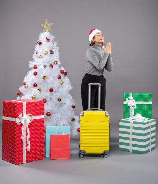 Donna che indossa il cappello di Babbo Natale con i bagagli accanto all'albero di Natale