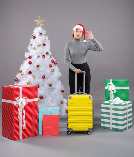 Donna che indossa il cappello di Babbo Natale con i bagagli accanto all'albero di Natale